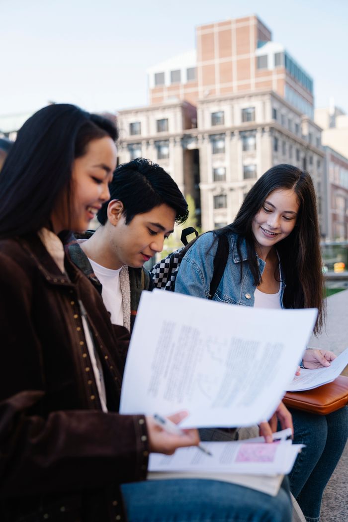 Home Group of young students reviewing documents outside a university building.