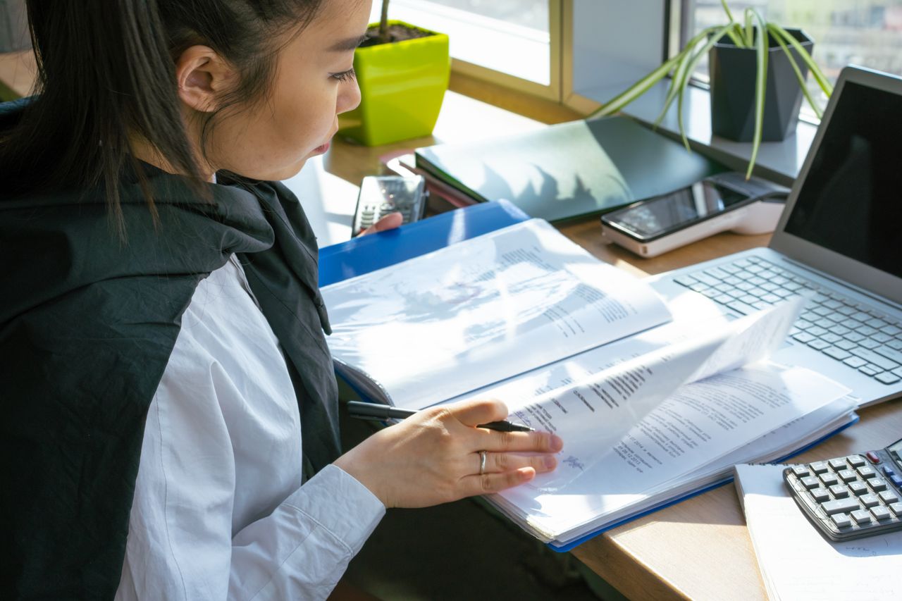 Focused woman reviewing documents at a desk with a laptop and stationery.